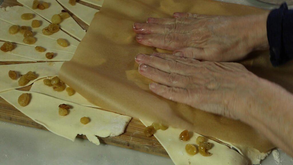 Raisins sprinkled on the dough, being pressed into the dough with parchment paper to make Rugalach